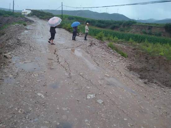 村民查看路况。山洪被堵在路的一侧，路面已经下沉。
