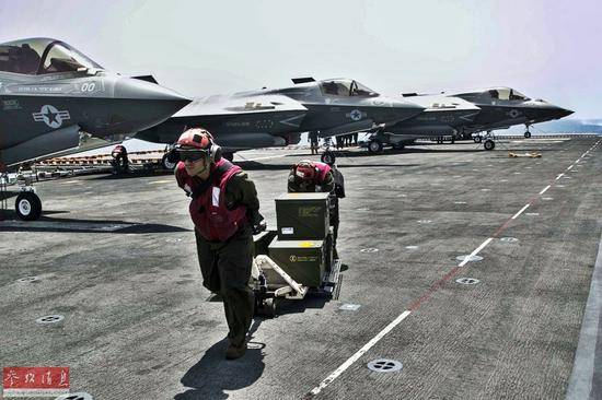 美海军军械官在飞行甲板上搬运弹药，背景可见3架F-35B战机。