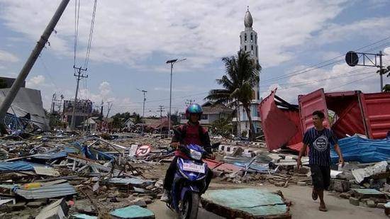 图为印尼帕卢当地居民骑车穿过布满碎片的街道。（图：法新社）