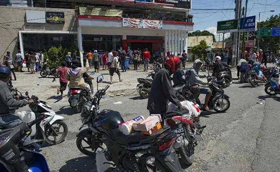 许多灾民骑着摩托车聚集到商铺门前。（图：法新社）