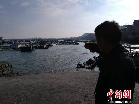 58岁的肖车明站在码头上，手指向不远处的自家渔排，对今后的日子充满无奈。陈龙山摄