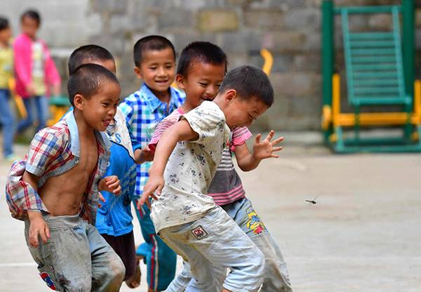 一所乡村学校内，孩子们在追逐蜻蜓。黄孝邦图