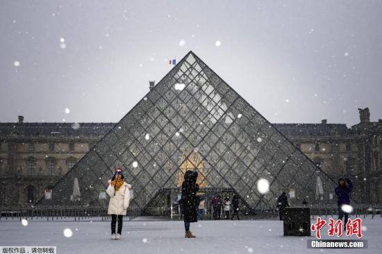 资料图片：当地时间1月22日，法国巴黎市中心降下2019年第一场雪。图为游客在卢浮宫前拍照。