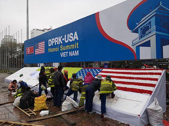 细雨绵绵中，现场的工人们正在使用假花拼组美国国旗。