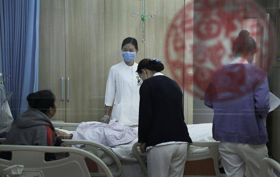2018年10月16日，北京大学首钢医院安宁疗护中心，一间病房里，三名护士及一名护工正在照顾一名病人。病房的落地窗上贴着一张福。新京报记者尹亚飞摄