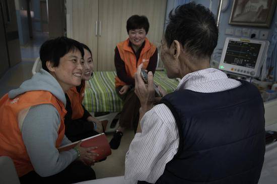 2018年10月16日，北京大学首钢医院安宁疗护中心，一间病房里，三名志愿者正在陪伴一名病人。他们用手机播放老歌，让病人或猜歌名或大家一起唱。这名病人来自广州，当志愿者跟他聊广州美食时，他特别开心。新京报记者尹亚飞摄
