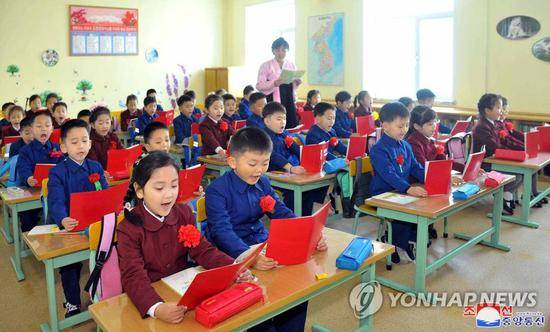 朝鲜一所学校里，小学生们戴着大红花，双手捧书认真朗读。（朝中社）