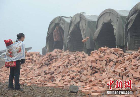 2009年1月2日，北川县一名妇女背着儿子接收解放军免费运送来的红砖，准备请人帮助重建家园。（中新社记者贾国荣摄）