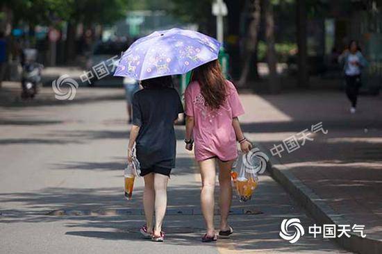 昨日北京街头晴热暴晒，市民打伞遮阳手拎冷饮。（图/王晓）