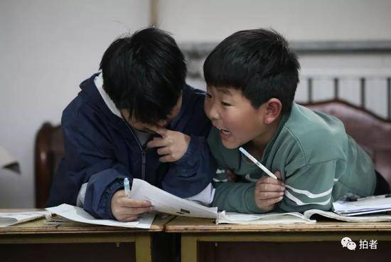 4月4日，河北涞水西官庄村，“小课桌”上，两位小朋友正在商量习题。新京报记者尹亚飞摄