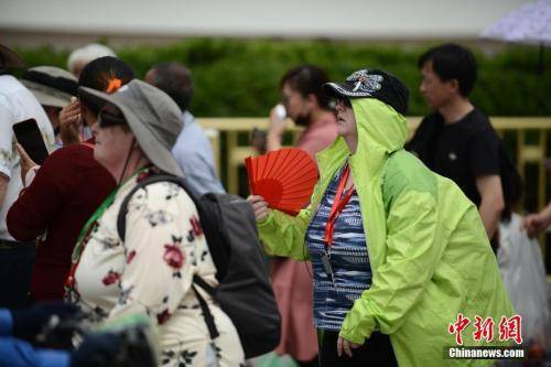  5月22日，在天安门前游玩的外国游客“花式”遮阳。中新社记者张兴龙摄