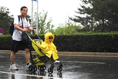 5月26日，天辰东路，一位市民冒雨推着童车前行，车上坐着“全副武装”的小朋友。新京报记者王飞摄