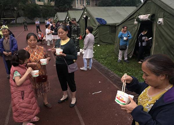  6月18日，在长宁县双河镇中学操场，群众吃上热粥。新华社图