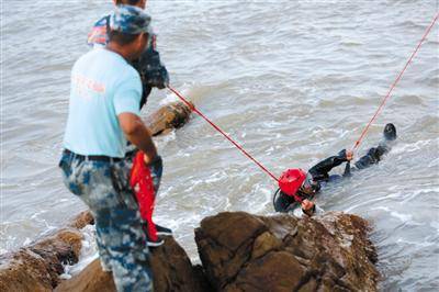 搜救中，队员们紧紧地拉着保护绳，以防潜水员被浪拍到礁石上受伤。