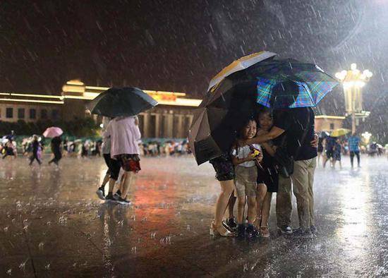 天安门广场，大雨中，游客抱作一团，孩子们却十分高兴。