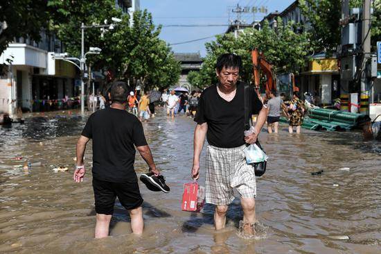 8月11日下午，临海部分路段仍有积水，一位市民在街上购买补给品后，趟水回家。新京报记者王嘉宁摄