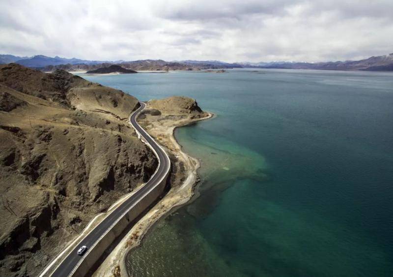 2016年4月28日，汽车沿着新藏公路班公湖畔的公路穿行，湖边依然隐约可见曾经崎岖泥泞的旧路（新华社记者江文耀摄）