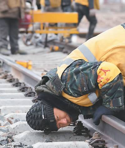 为确保青藏铁路唐古拉线路火车在春运期间安全通行，上百名线路工、劳务工坚守在这里，顶狂风战暴雪，排除冻土、大风、塌方等危害铁路安全的险情。图为2019年1月28日，工人跪伏在铁轨上观察铁轨水平高度。新华社记者周健伟摄