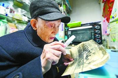 这张泛黄的老照片是1954年北京航空航天大学飞机设计系成立时的教职工合影，文传源用放大镜仔细端详，寻找年轻时的自己。