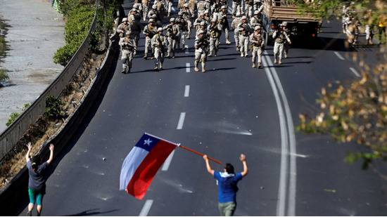 抗议期间，智利士兵聚集在示威者附近，其中一人举着智利国旗。图源：路透社