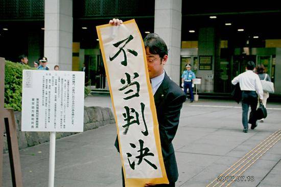 2007年7月18日，日本东京高等法院门口，一名律师举着“不当判决”的竖幅文字。
