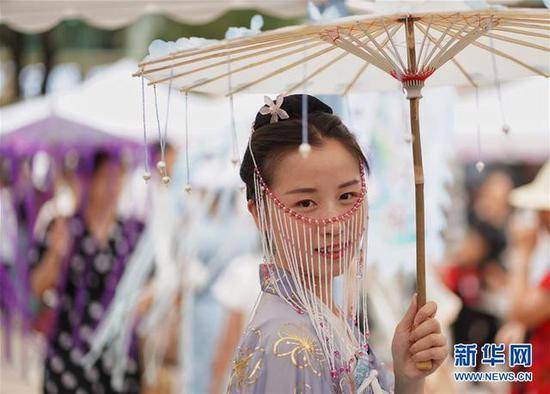 云南省昆明市，身着传统服饰的女孩手撑纸伞参加七夕节特别活动。