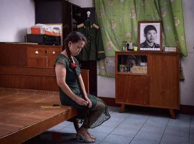 李正萍坐在卧室里，对着丈夫的照片静静地梳理着一头长发。