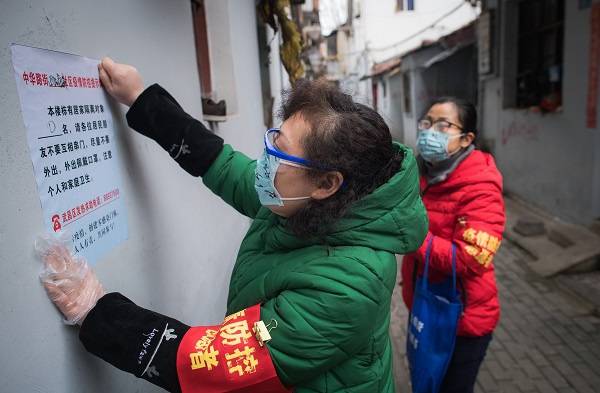  2月7日，在离武汉著名景点黄鹤楼不远的中华路街道西城壕社区，社区网格员曹岚英（左）在张贴防疫提示。新华社图