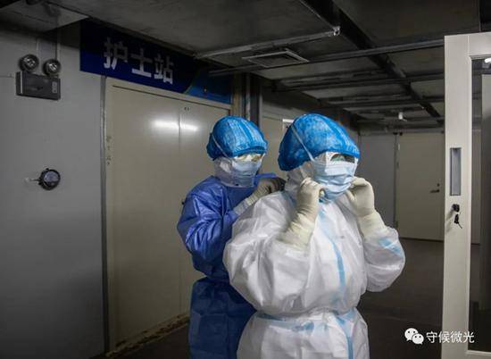 2月21日，武汉火神山医院感染八科护士站门前，该病区的护士长左卉川（右）在护理部助理员葛雪燕的帮助下戴上第二层口罩。中青报·中青网记者李峥苨/摄