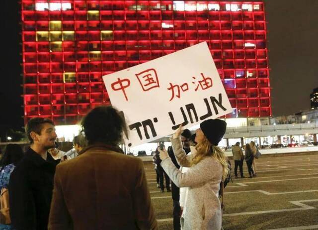 2月11日，在以色列特拉维夫市政大楼前，一名女子手举带有“中国加油”字样的宣传板，宣传板上用希伯来语写着“我们在一起”。新华社发（吉尔·科恩·马根摄）