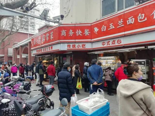 2月19日，上海一家包子铺前，顾客们“全副武装”排队购物。店前排队人数逐步回升。受访者供图