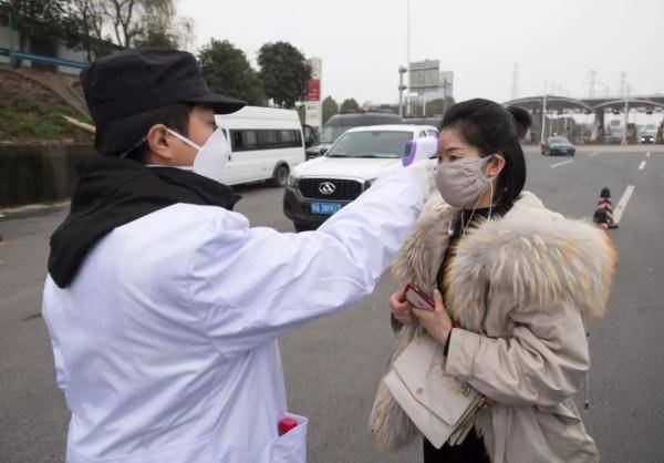 ↑1月23日，在武汉武鄂高速龚家岭收费站，工作人员对进城旅客进行体温检测。图据新华社