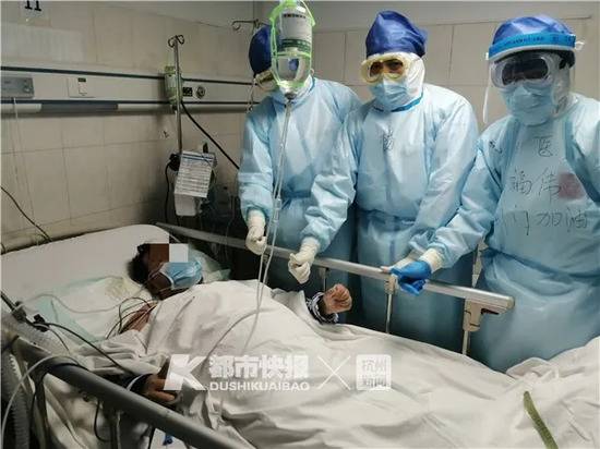 荆门首例ECMO患者成功撤掉呼吸机，在病床上竖起大拇指，和医护人员合影。