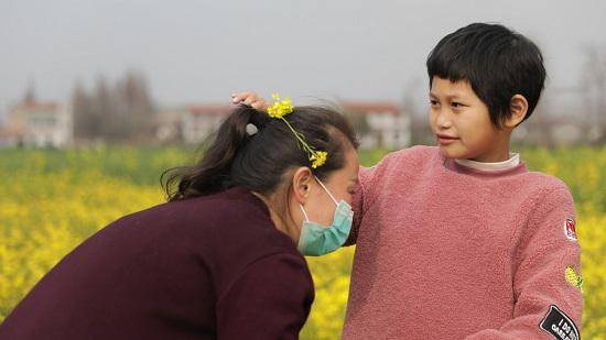 开心将油菜花插在了妈妈头上。