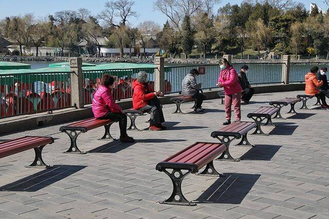 在湖边休息的几位游客散坐在不同的长椅上“远距离”聊天。