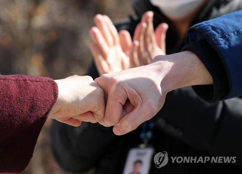 韩国治愈并解除隔离的新冠患者在离开生活治疗中心前与医务人员击拳告别。（韩联社）