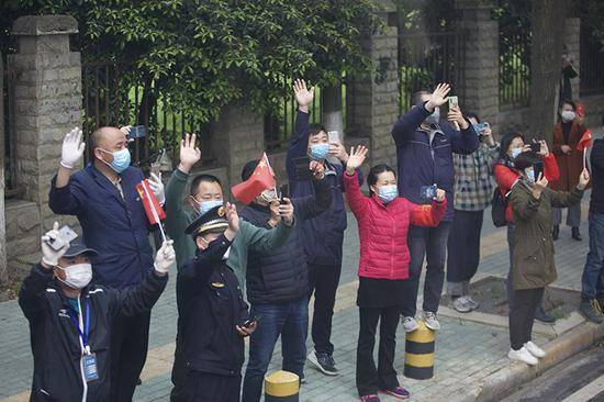 武汉市民在道路旁与医疗队挥手道别。