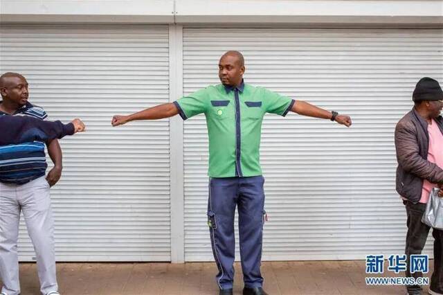 ▲3月30日，在南非约翰内斯堡，一名便利店工作人员举起双臂，让排队购物的市民保持距离。受疫情影响，南非已经实施全国范围“封城”。新华社发（耶希尔摄）