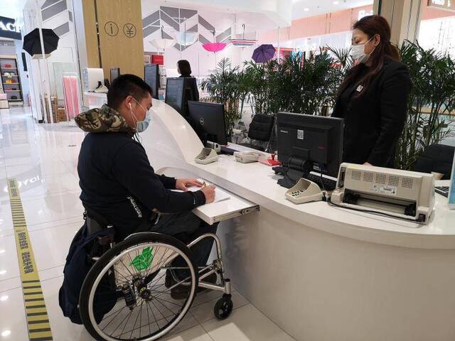 潘逸飞在为轮椅人士专设的低位服务台前填写服务单。摄影/新京报记者黄哲程