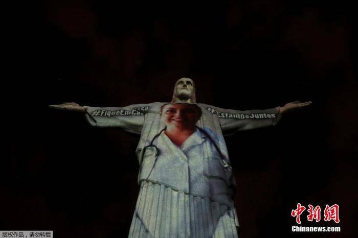 资料图：当地时间4月12日，巴西里约热内卢的耶稣雕像穿上了“白大褂”，雕塑上用多国语言向在抗击新冠肺炎一线工作的医护人员表示感谢。