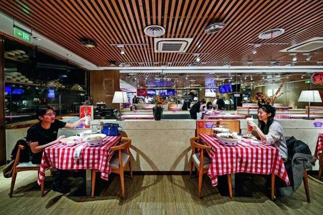  3月11日，一对情侣在天津大悦城内一家餐厅隔桌而坐就餐。当日，天津部分商场恢复营业，运营期间将不间断地进行公共区域高频定时消毒并限制客流。摄影/本刊记者佟郁