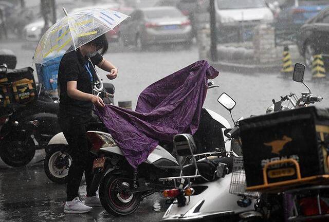 16时05分，广渠路，行人雨中遮盖电瓶车。