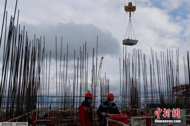 资料图：俄罗斯莫斯科，在放松了封锁限制后，建筑工人们戴着口罩在一幢摩天大楼上工作。