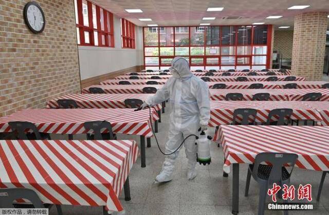 资料图：当地时间5月11日，韩国，首尔一所高中的食堂里，一名身穿防护服的卫生官员正在喷洒消毒剂。