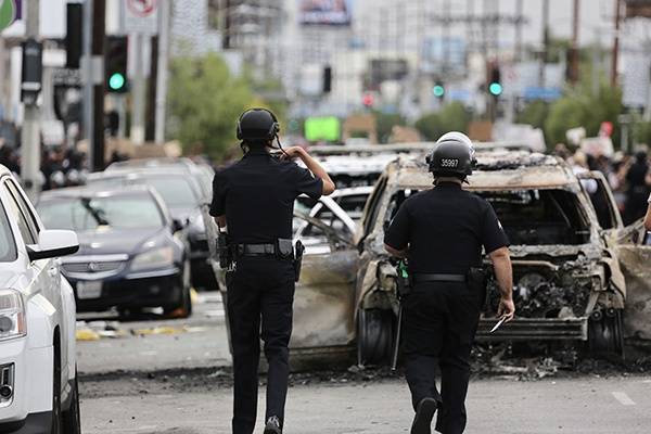 5月30日，在美国洛杉矶，警察走向被烧毁的车辆。新华社图