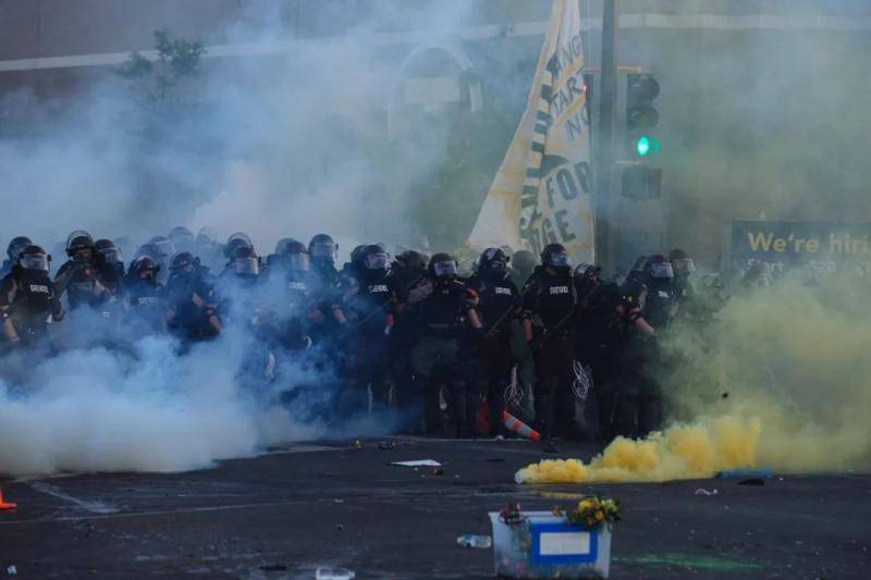  5月30日，在美国明尼苏达州明尼阿波利斯市，警察经过一片催泪瓦斯覆盖的区域。新华社发（安格斯·亚历山大摄）