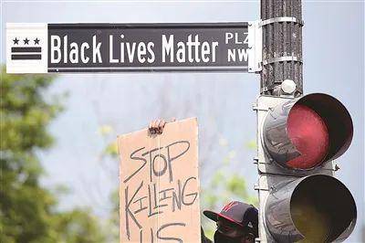 6月6日，一名男子手举“停止杀害我们”的标语在美国华盛顿白宫附近的“黑人的命也是命广场”路牌下参加游行活动（新华社记者刘杰摄）