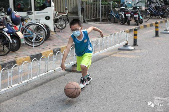 △6月20日，戴着口罩练球的男孩。封闭的小区少了车来车往，路上也能成为运动场。