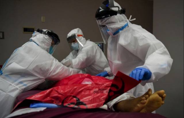 △医护人员用白布盖住病人的尸体，并将其包裹在一个生物危害袋里。图片来源：路透社