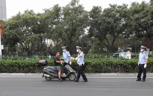 一名摩托车驾驶员因为没戴头盔被民警拦停。摄影/新京报记者王贵彬